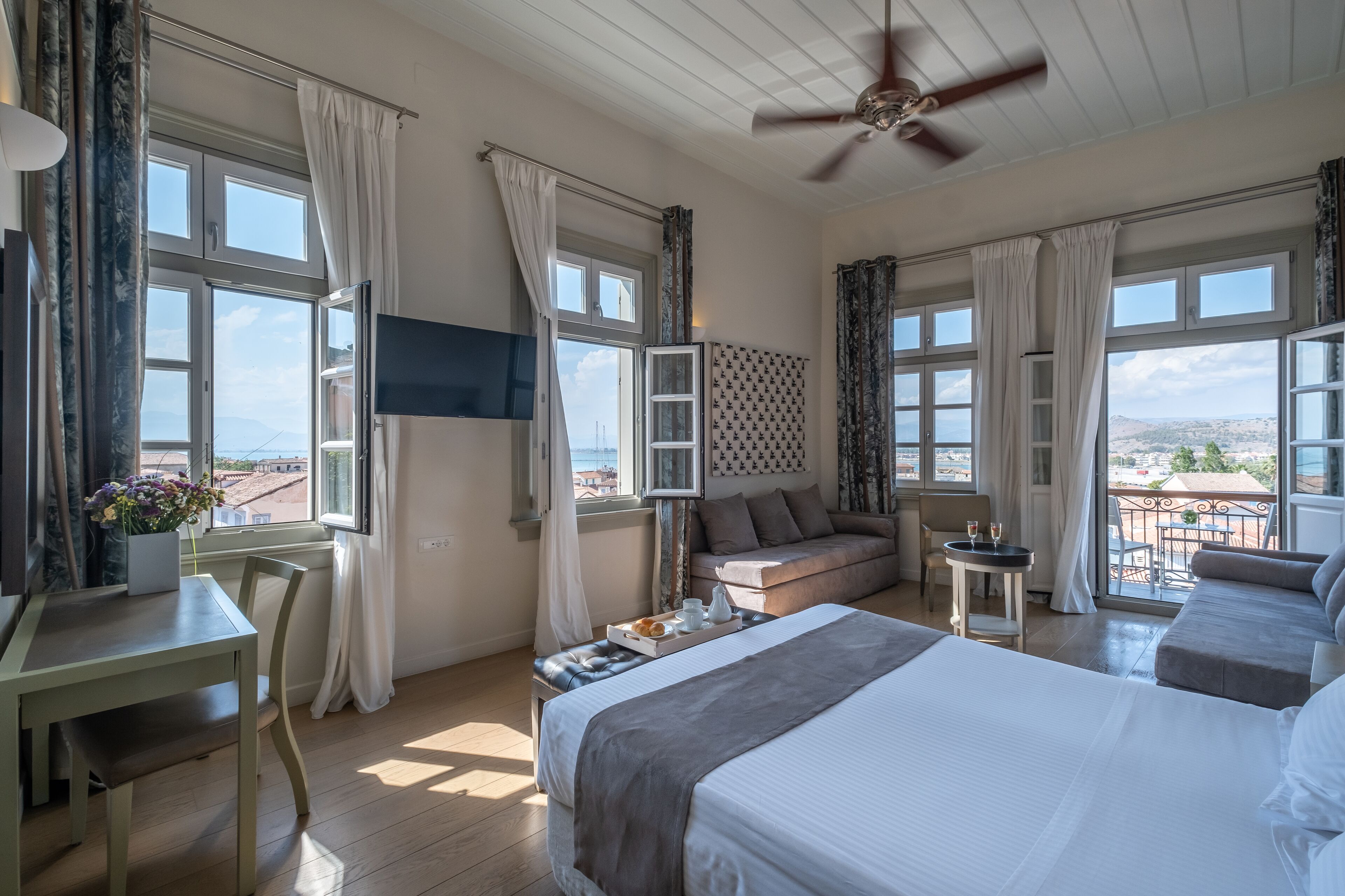 A hotel room with a bed, a desk, a chair, a sofa, and a balcony with a view.