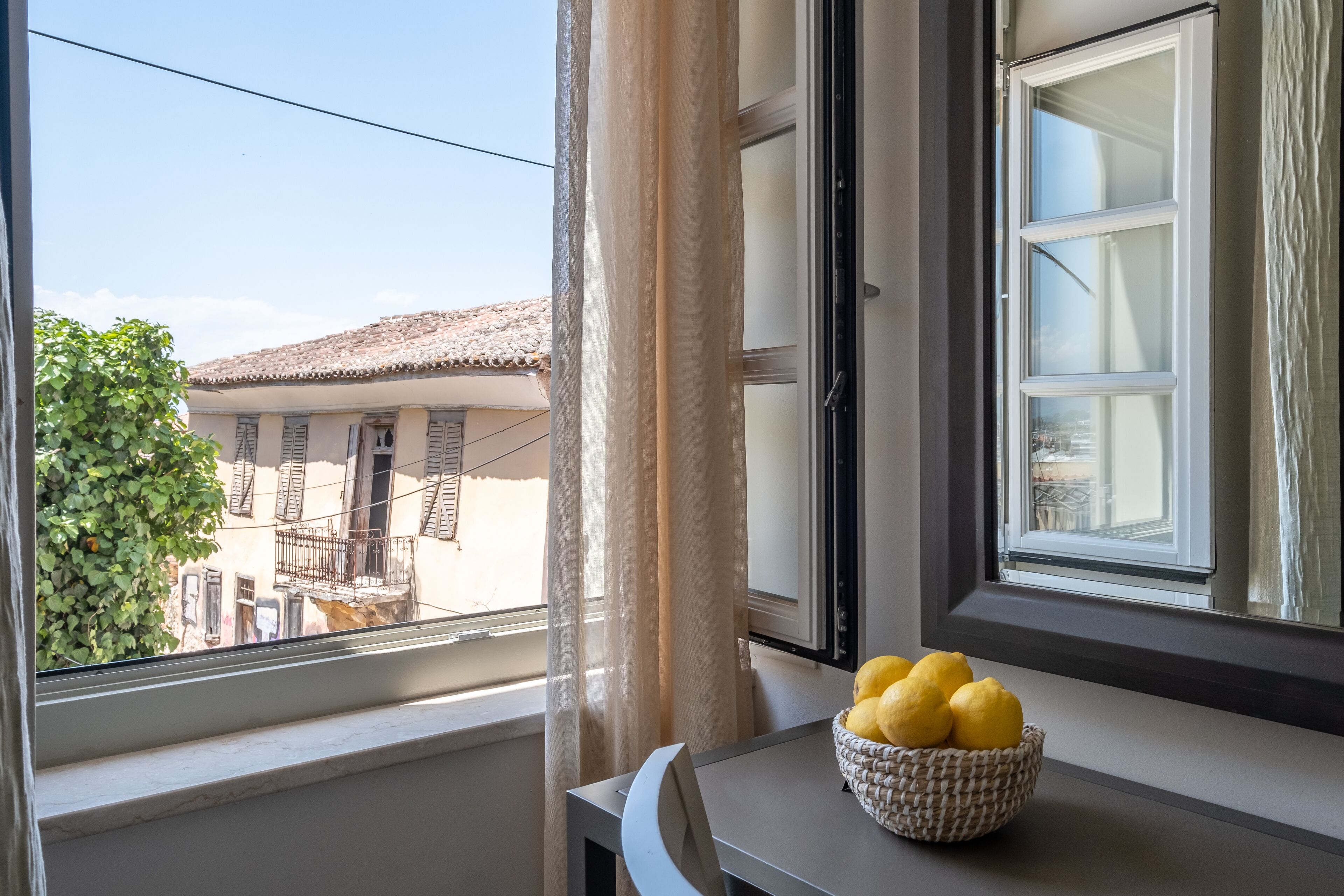 A window with a view of a building and a basket of lemons on a table.