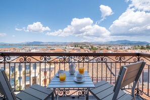 Un balcón con una mesa dispuesta para el desayuno, con vistas a un paisaje urbano que incluye edificios y montañas.