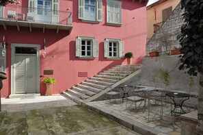Un edificio rosa con contraventanas blancas, una escalera y asientos al aire libre.