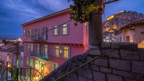 A pink building with multiple windows and balconies, a stone staircase, and a view of a hill with lights. - Grand Sarai Nafplio (Nafplio)
