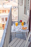 Un balcón con una mesa dispuesta para el desayuno, que incluye croissants, jugo y un florero con una rosa.