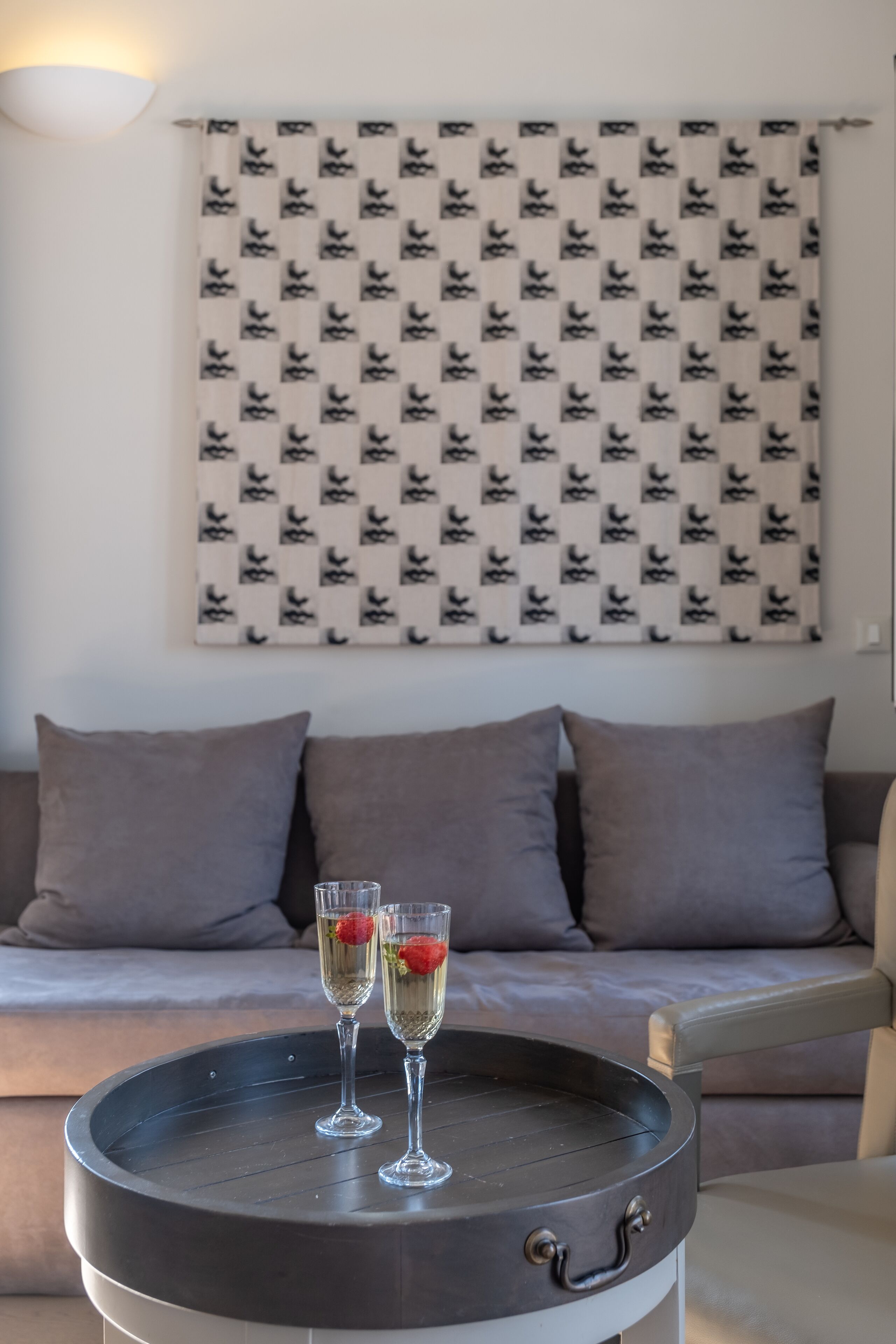 A modern living room with a round coffee table, two champagne flutes with strawberries, a sofa, and a patterned wall hanging.