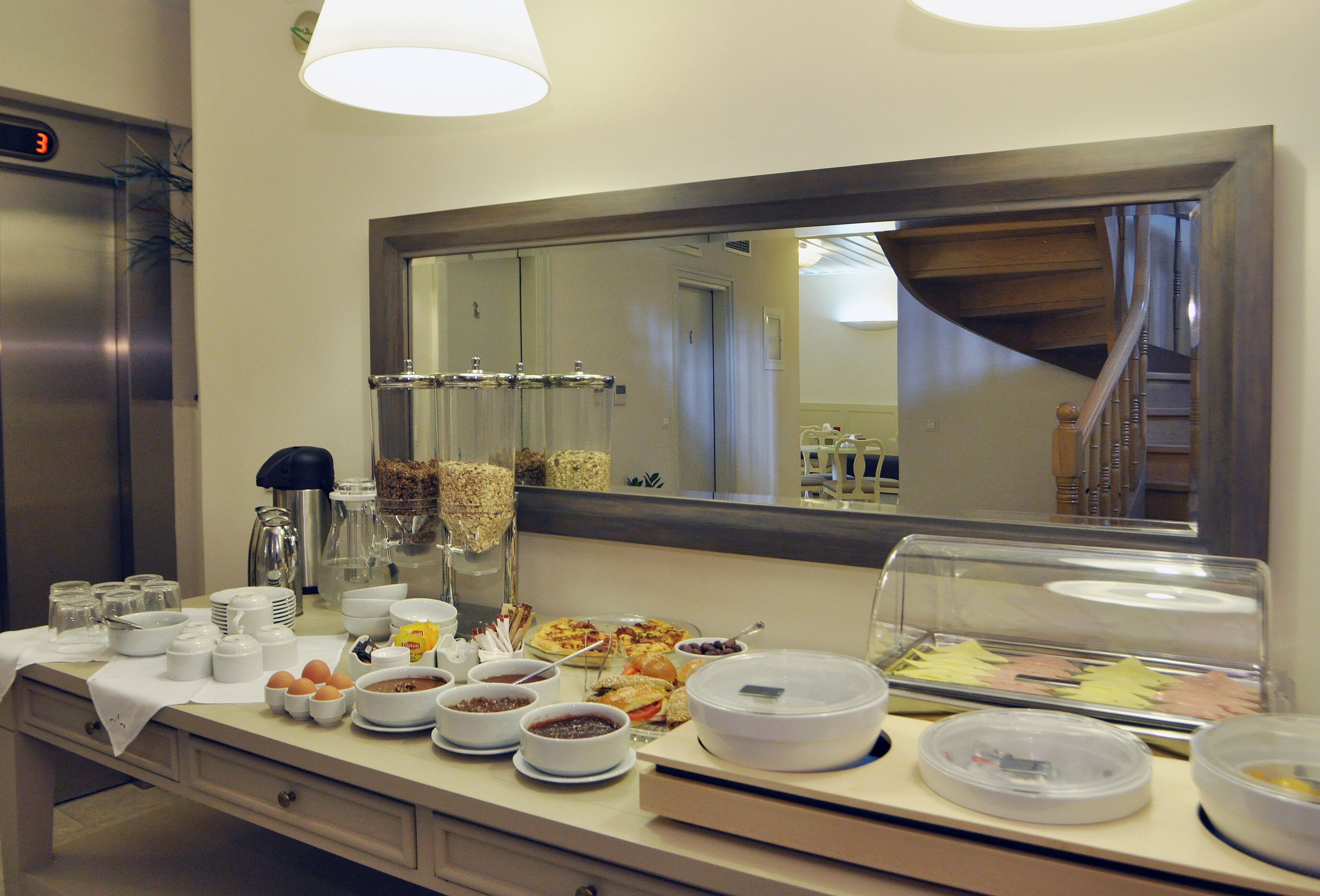 A buffet setup with various food items and containers, a digital clock, and a mirror reflecting the room.