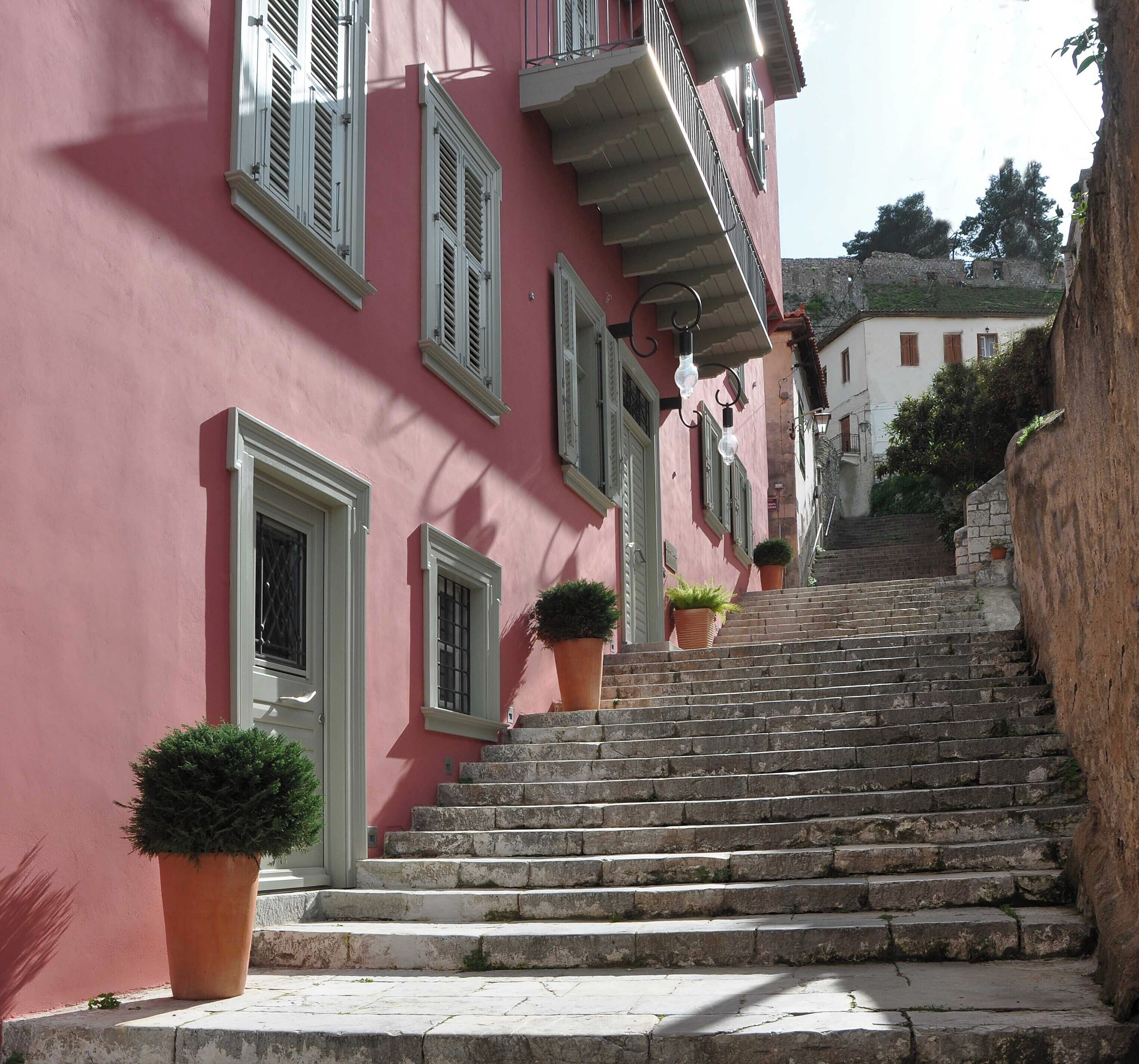 A pink building with white shutters, stone steps, and potted plants.