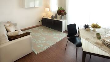 A modern living room with a sofa, a dining table set with a vase of flowers, and a cabinet with a lamp.