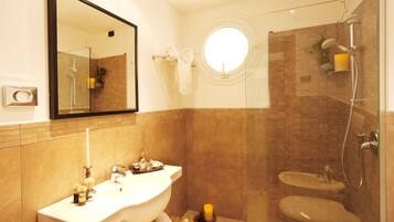A bathroom with a large mirror, a round window, a sink, and a shower area.