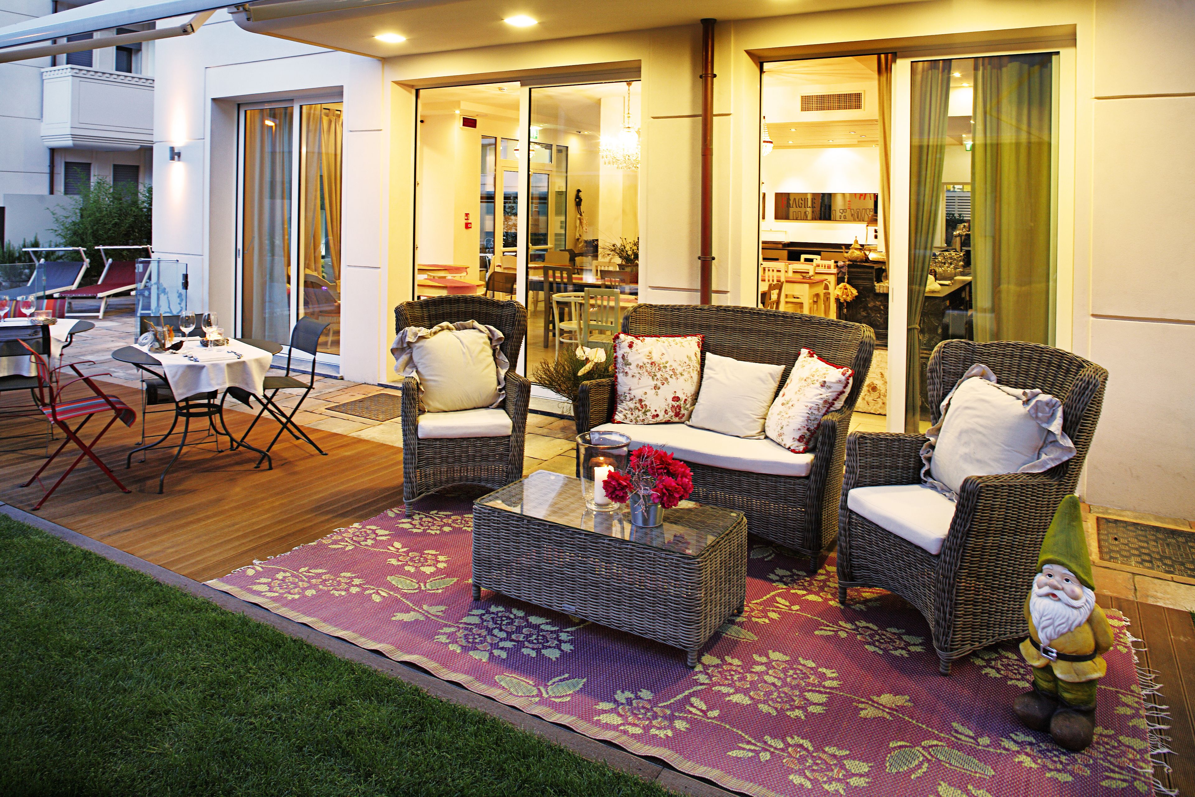 An outdoor seating area with wicker furniture, a glass-top coffee table, and a decorative gnome.