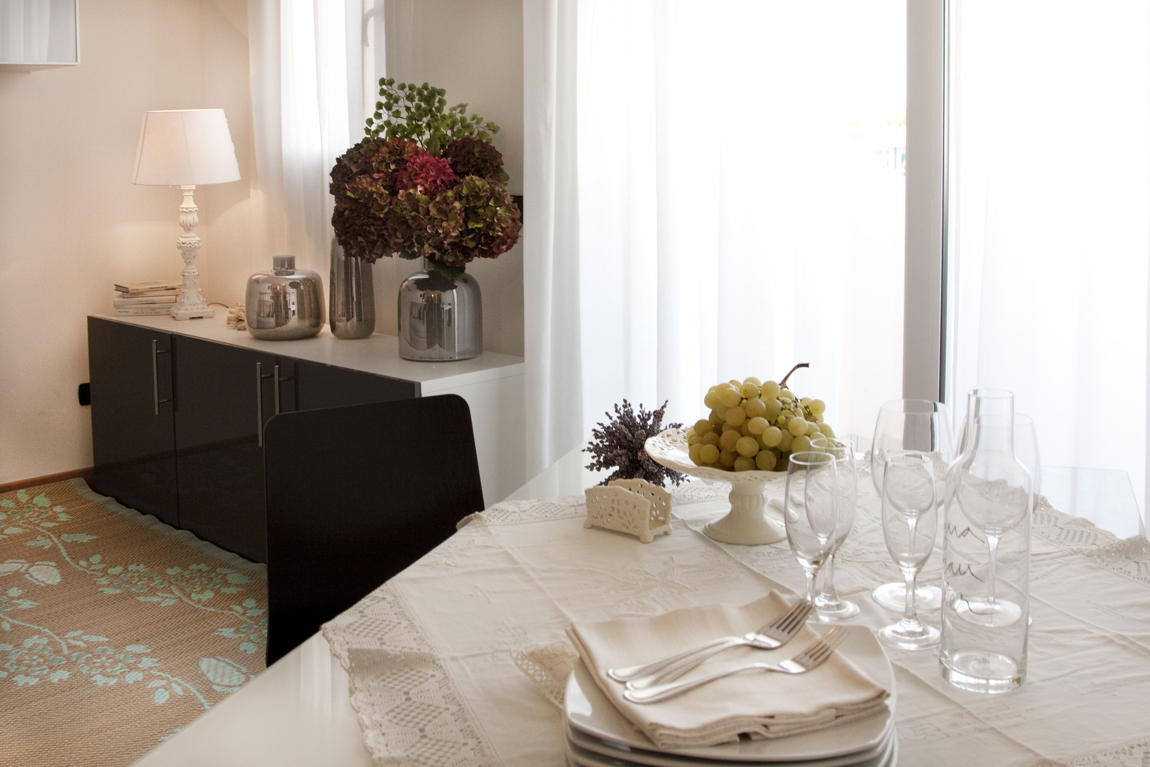 A dining area with a table set for four, a vase with flowers, and a fruit bowl.