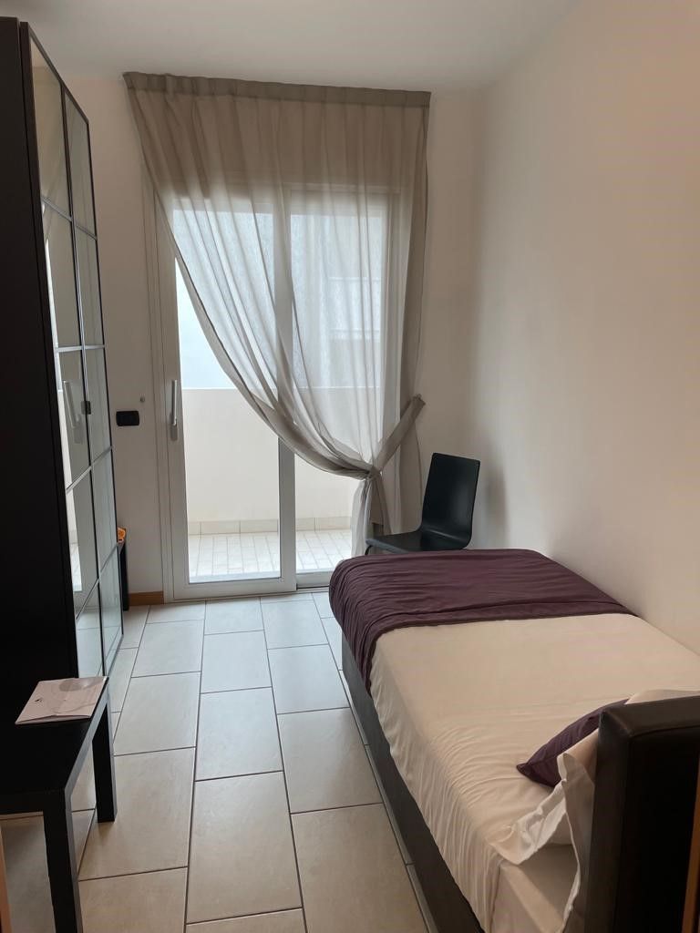 Ein Schlafzimmer mit Bett, Sessel, Kleiderschrank und einer Glastür zum Balkon.