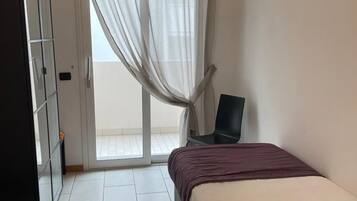 Ein Schlafzimmer mit Bett, Sessel, Kleiderschrank und einer Glastür zum Balkon.