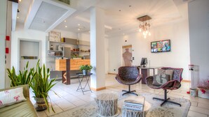 Una sala moderna con un sofá, dos sillones, una mesa de centro y un televisor. Se observa una zona de cocina al fondo.