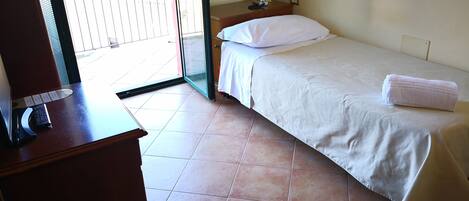 A hotel room with a bed, a desk with a telephone, and a view of the outside balcony.