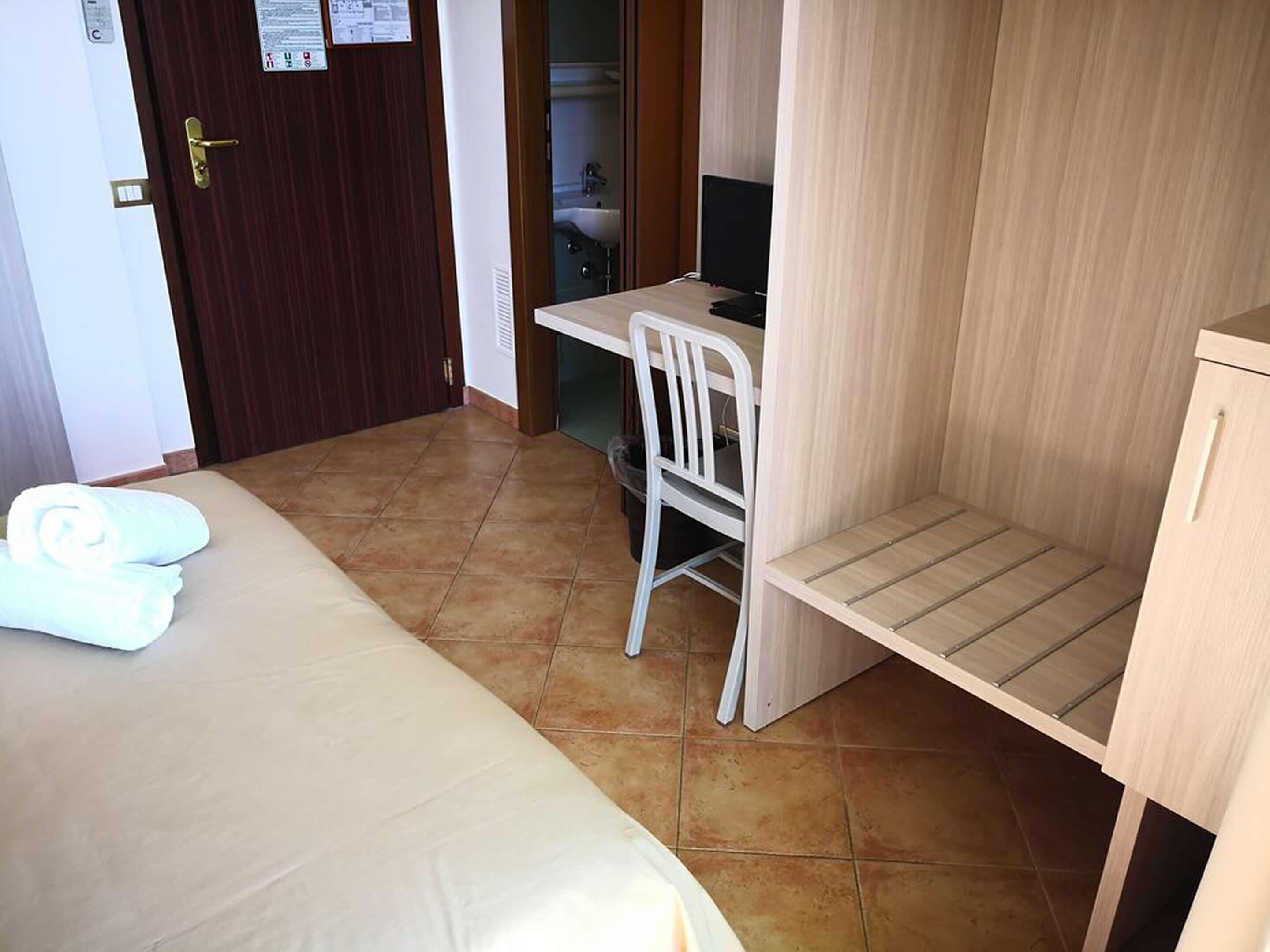 Una habitación de hotel con cama, escritorio, silla y una pequeña estantería.