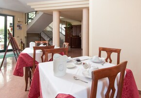 Zona pranzo con tavoli apparecchiati per il tè, sedie di legno e una scala sullo sfondo.