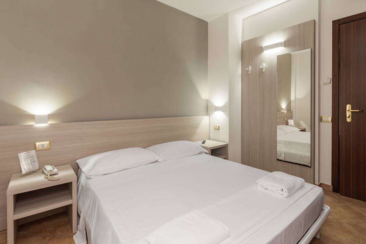 A hotel room with a large bed, bedside tables, a mirror, and a door.