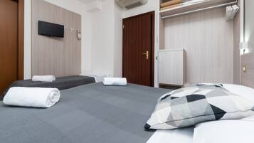 A hotel room with a bed, a TV mounted on the wall, a wardrobe, and a small cabinet.