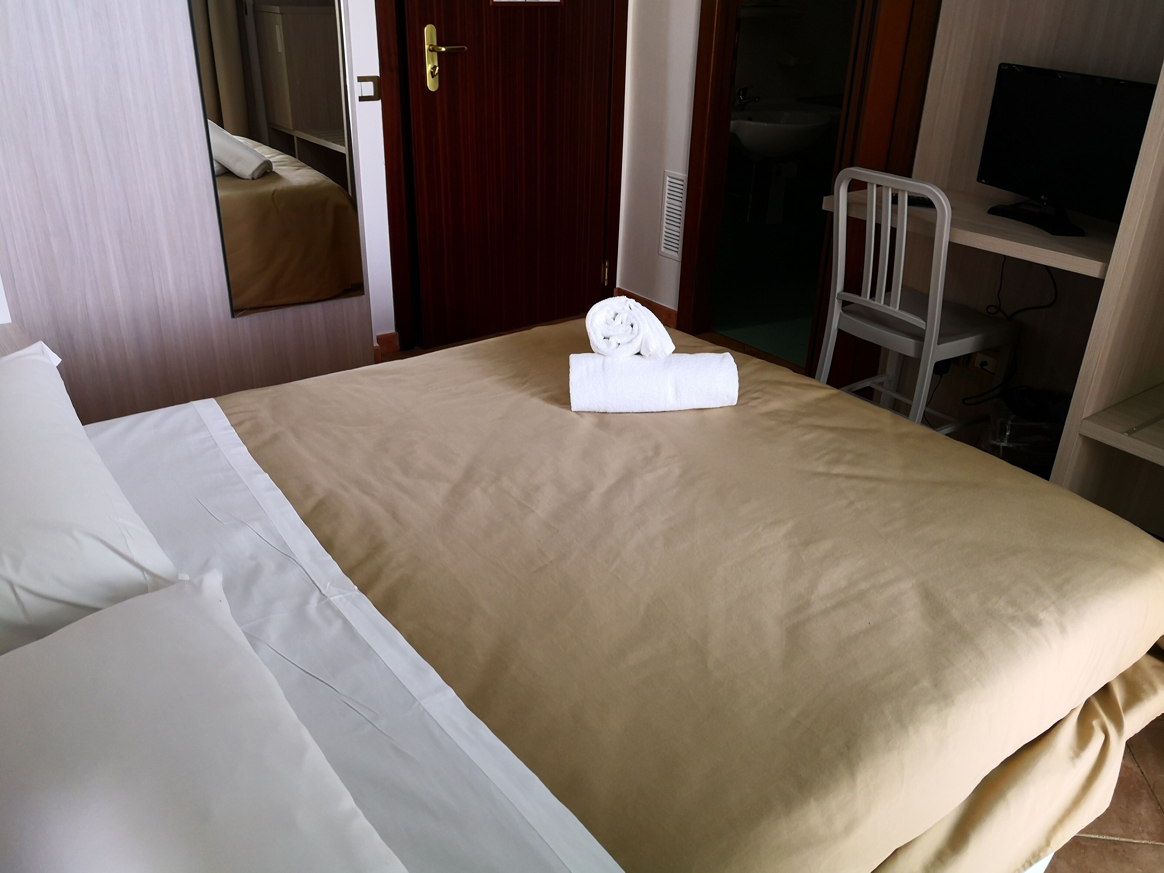 A hotel room with a bed, a folded towel, a television, and a chair.