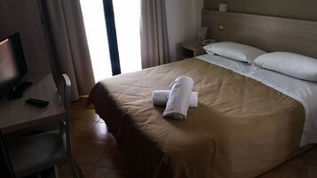 Une chambre d’hôtel avec un lit, un bureau avec un ordinateur, une chaise et une fenêtre avec des rideaux.