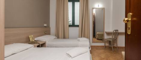 Ein Hotelzimmer mit zwei Betten, einem Schreibtisch, einem Stuhl, einem Spiegel und einem Fenster mit Vorhängen.