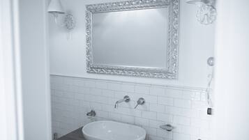 Un bagno con un lavandino bianco, due rubinetti, uno specchio con cornice decorata e un portalampada a parete.