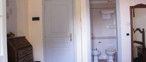 Un dormitorio con cama, cómoda de madera, una puerta y baño con inodoro y bidé.