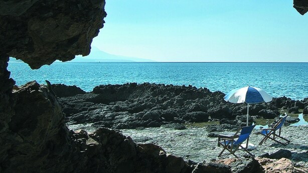 A rocky beach with a cave opening to the sea, two blue and white beach chairs, and a single umbrella. - Hotel Villa delle Meraviglie (Maratea)