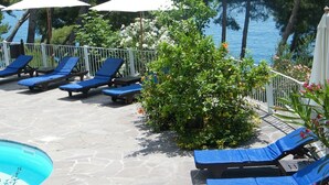 A poolside area with lounge chairs and umbrellas, a stone floor, and a view of the sea. - Hotel Villa delle Meraviglie (Maratea)