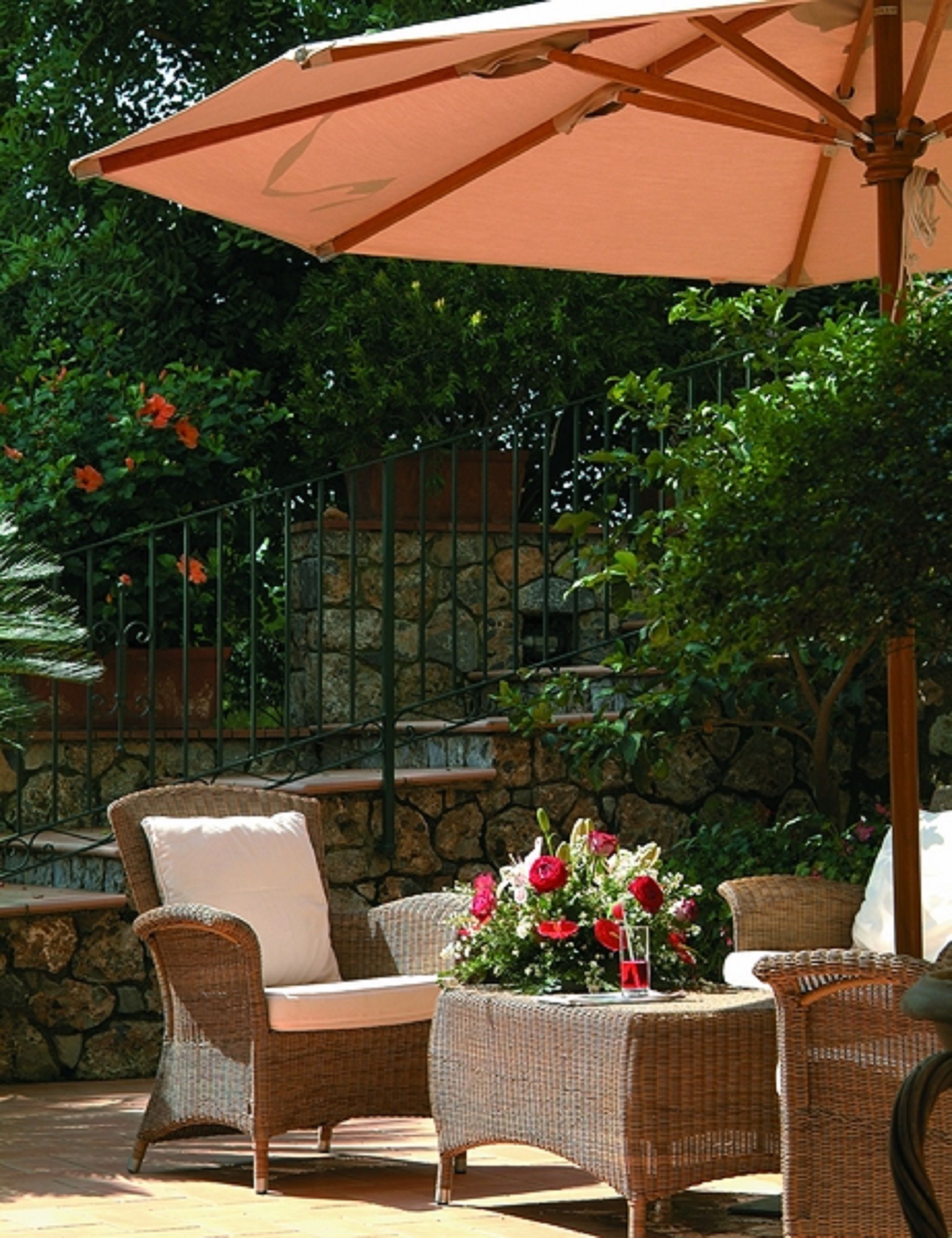 An outdoor patio area with wicker furniture, a table with a floral centerpiece, and a large umbrella.
