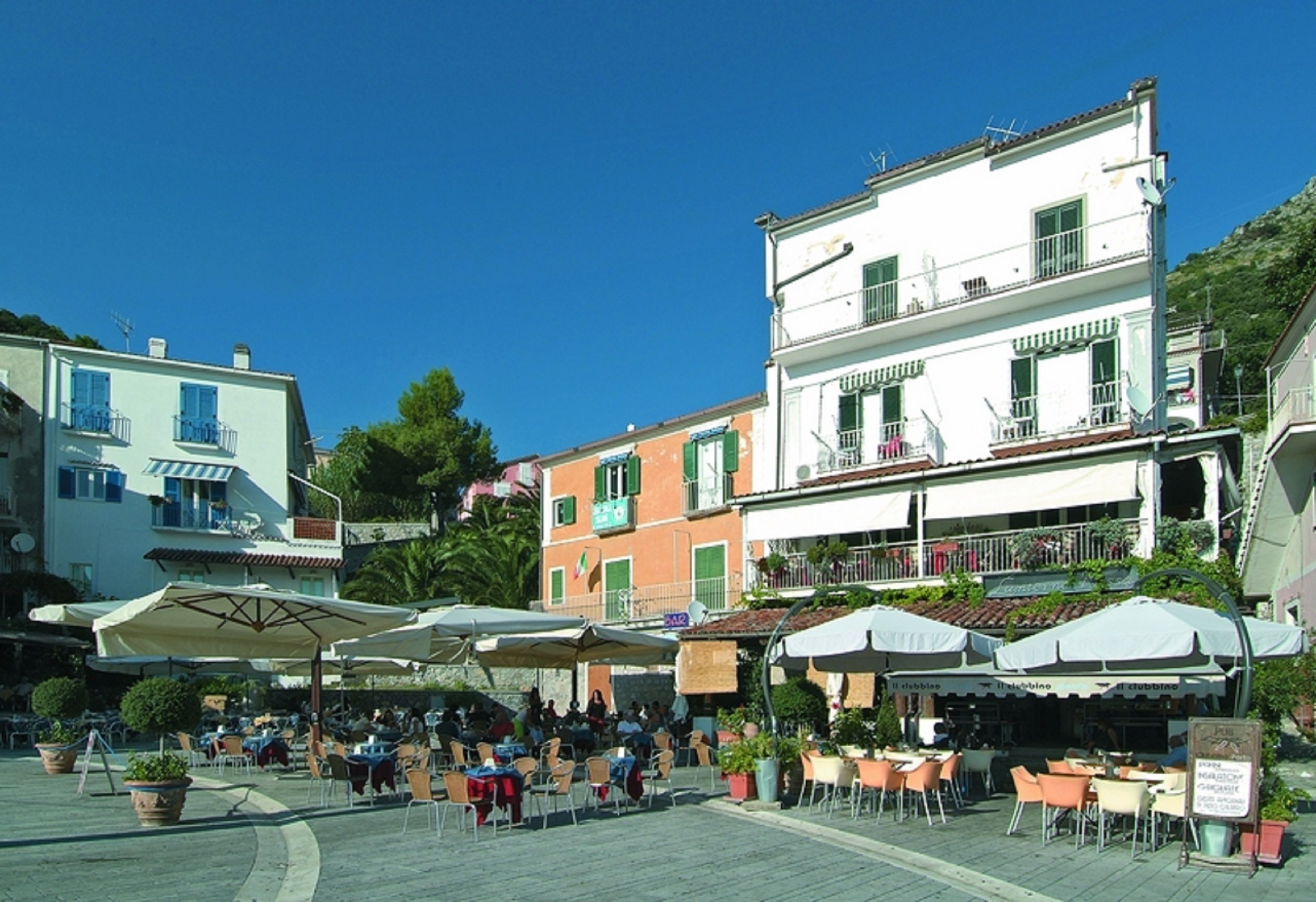 A square with outdoor seating, surrounded by colorful buildings with balconies and awnings.