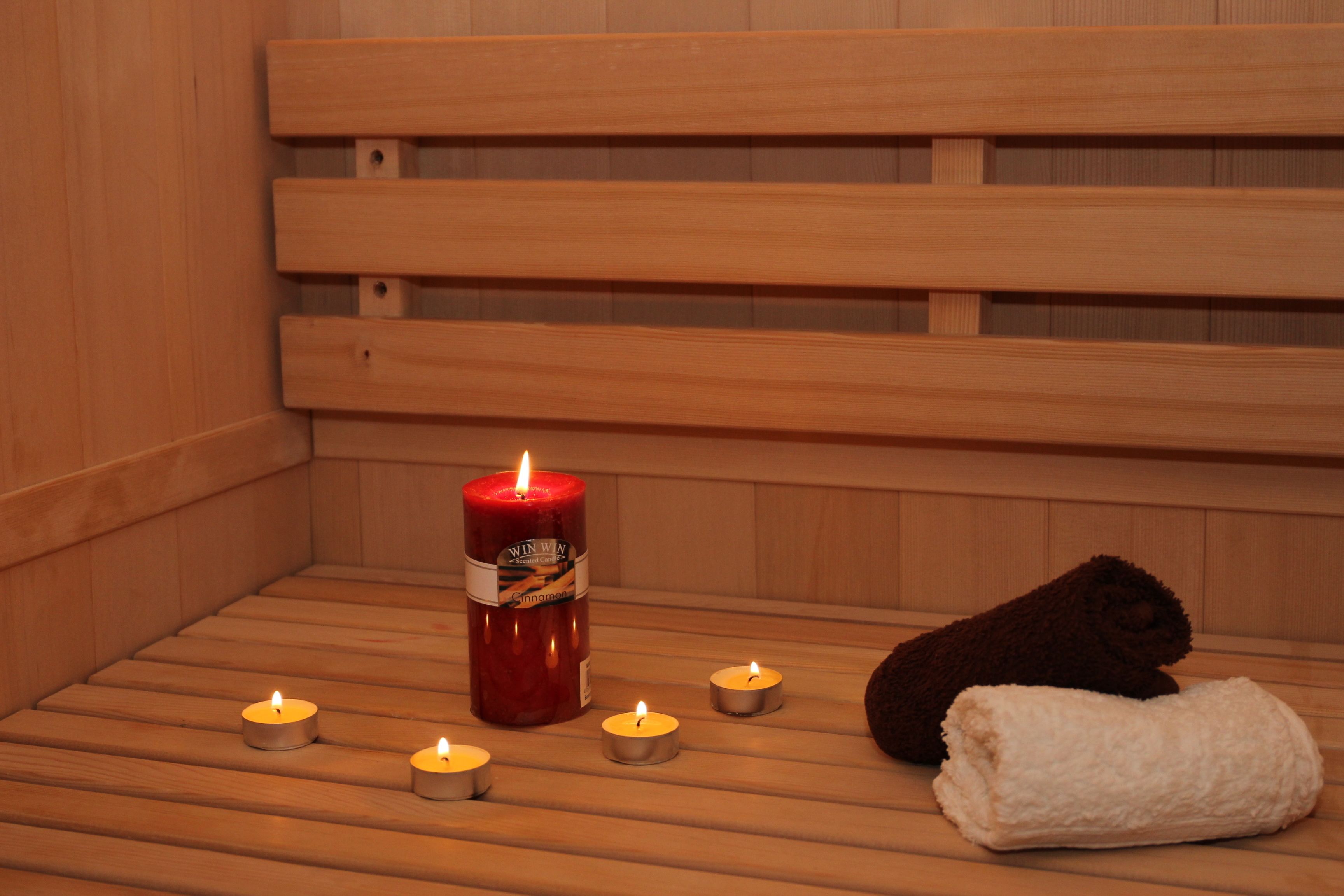 A wooden sauna with a large red candle, smaller candles, and a rolled towel.