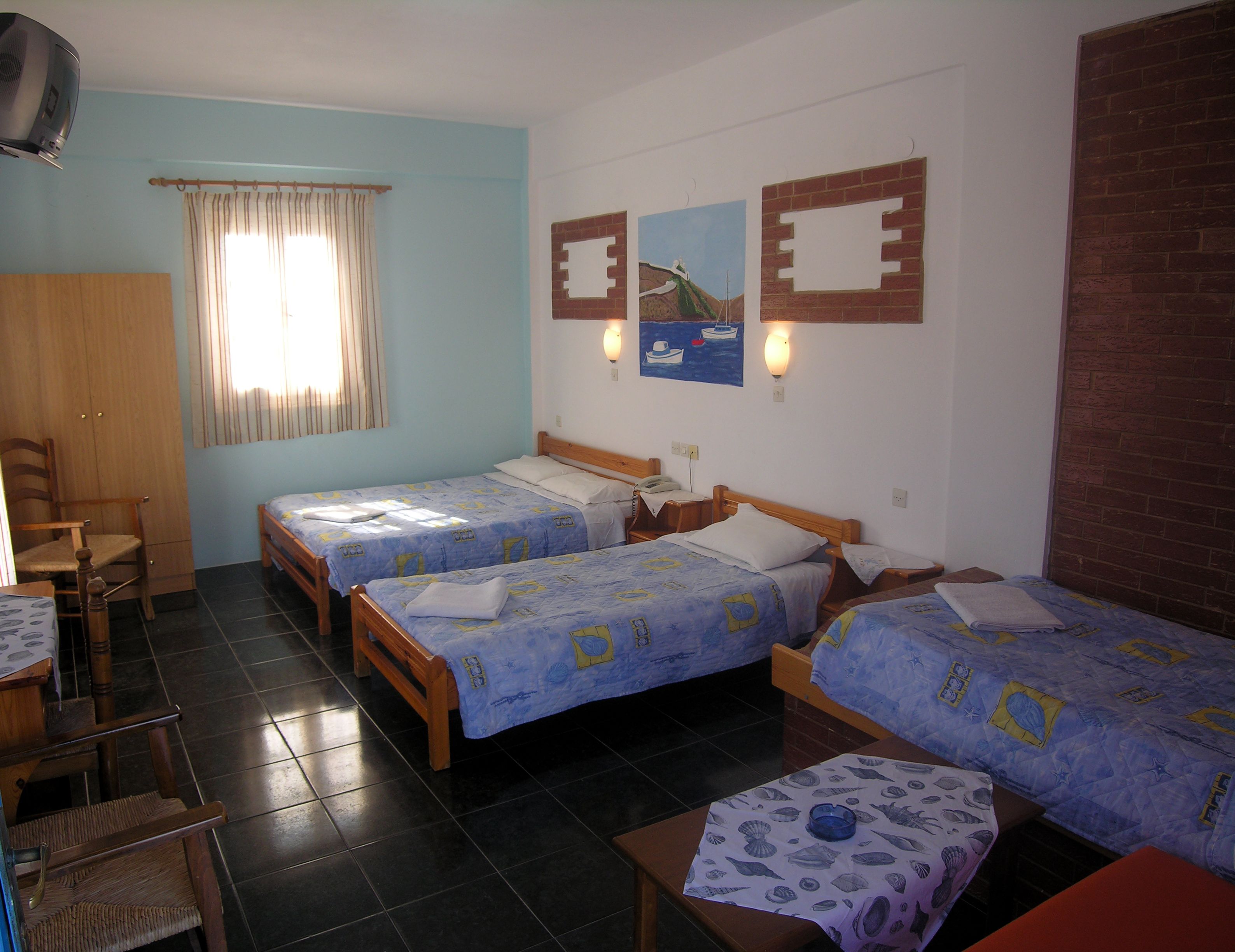 A room with two beds, a wooden wardrobe, a chair, and a table.