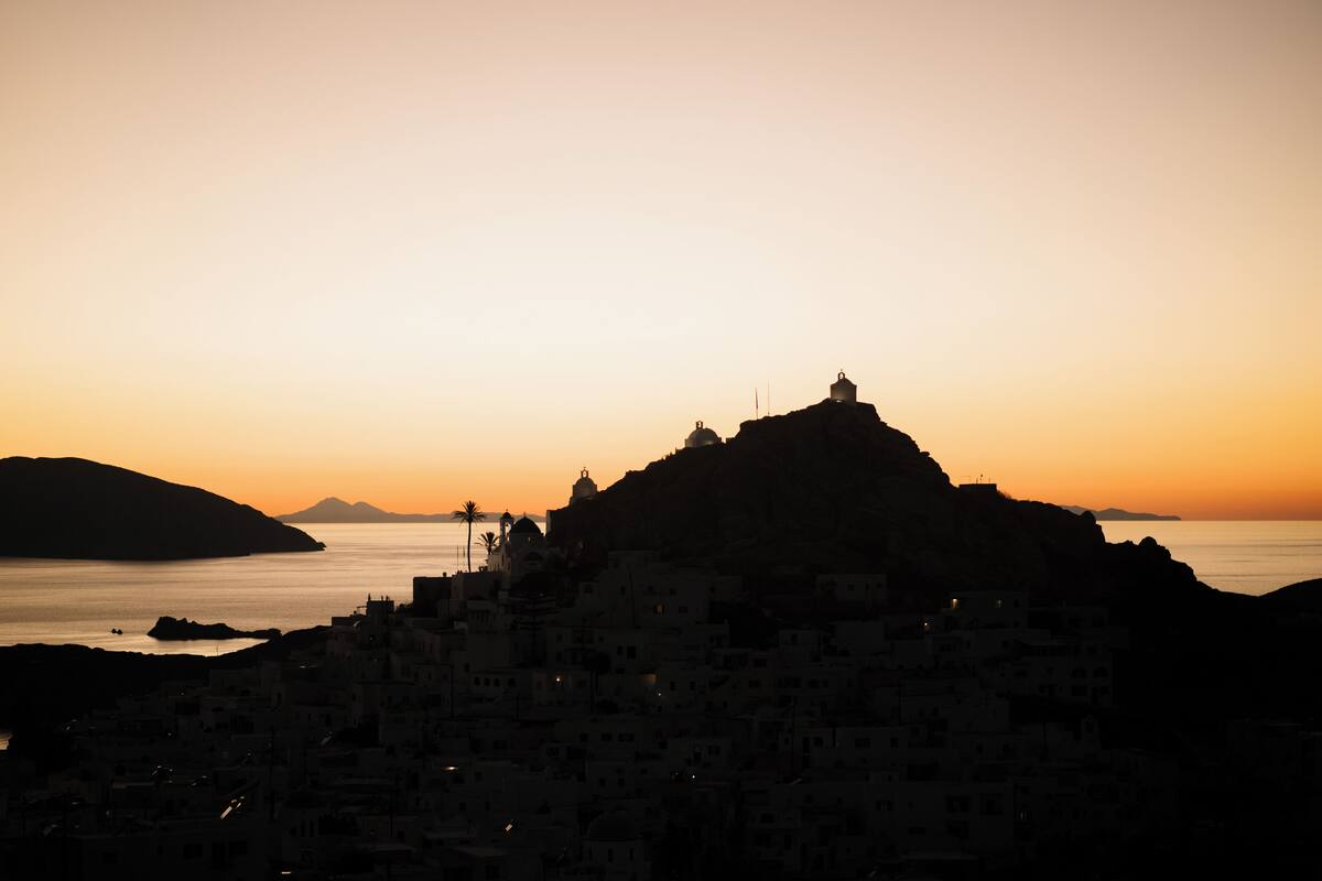 A coastal town silhouette at sunset with buildings clustered around a hill.