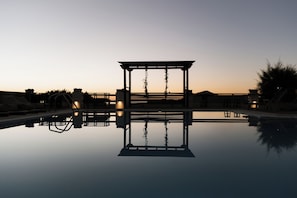 A serene pool area with a pergola structure, surrounded by potted plants and a clear sky. - Skala Hotel (Ios)