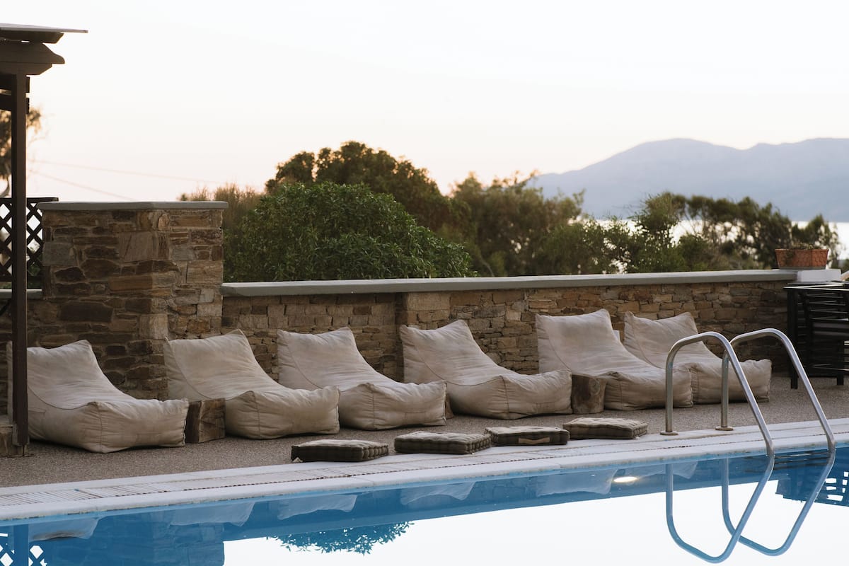 A poolside area with stone walls, beige cushions, and a metal ladder.