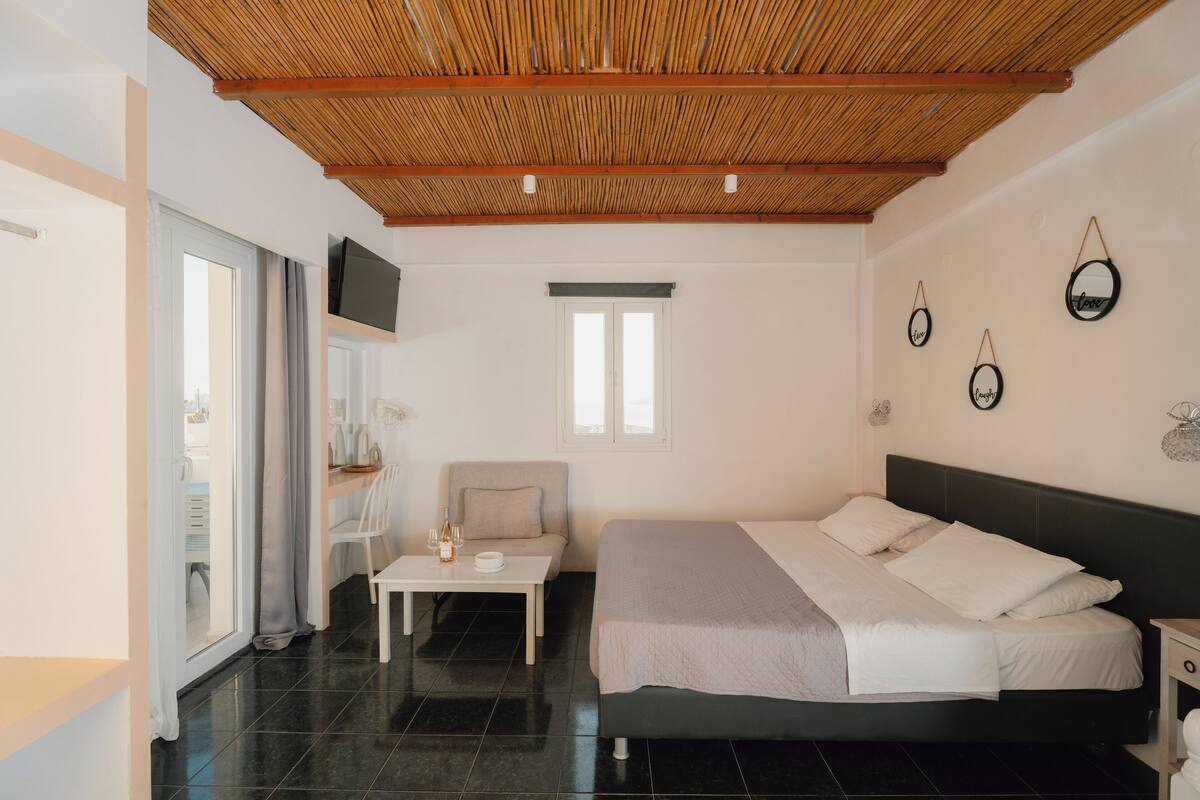 A bedroom with a bed, a TV mounted on the wall, a window, and a door.