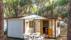 A small, single-room cabin with a table and chairs outside, a door leading inside, and a number '109' on the wall. - Camping Village Baia Blu La Tortuga (Aglientu)
