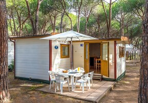 Una cabaña pequeña de una sola habitación con una mesa y sillas afuera, una puerta que da al interior y el número '109' en la pared.