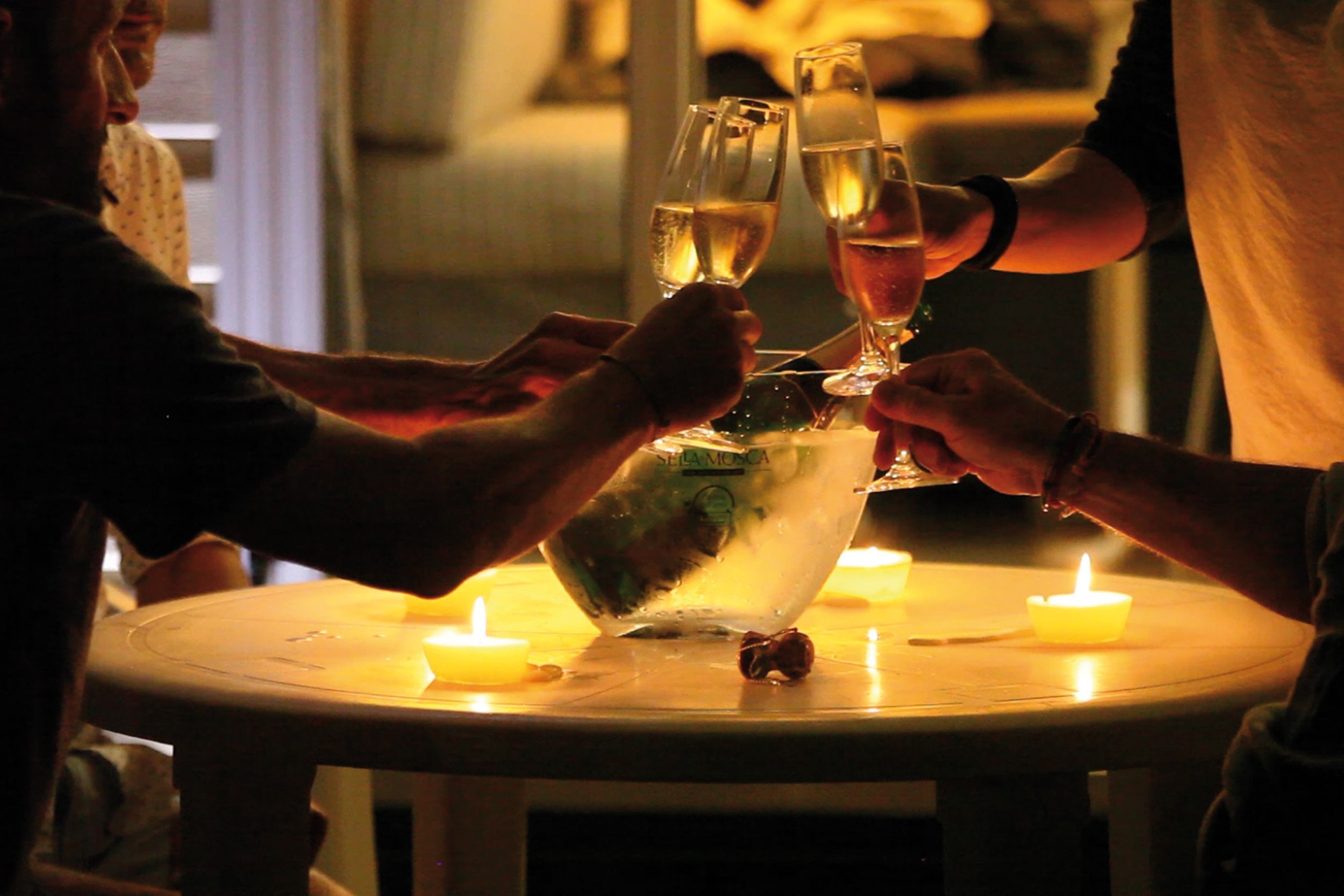 A round table with a bottle of water, two glasses of wine, and a lit candle.