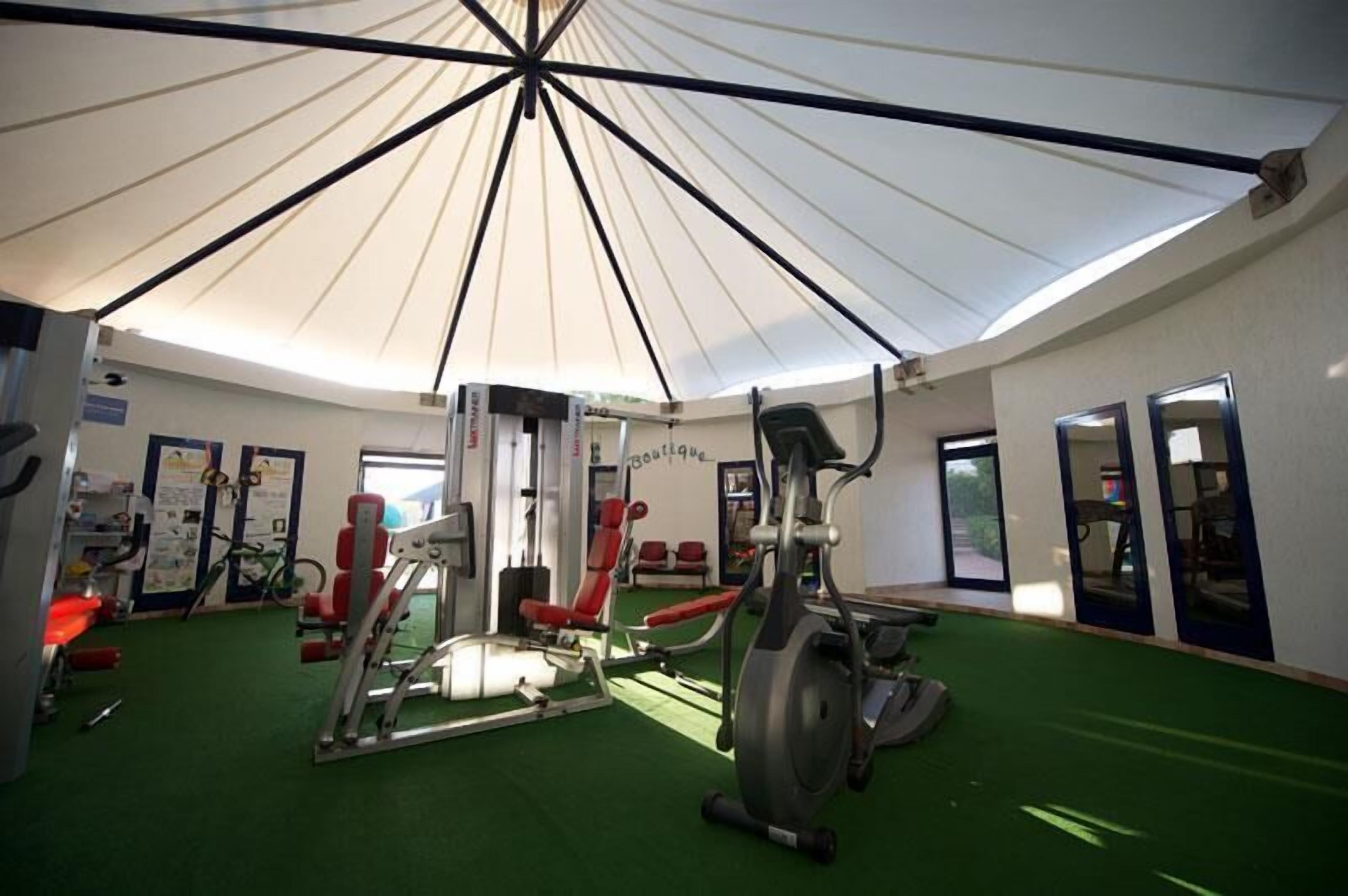 A gym with exercise equipment, a green carpet, and a large white ceiling fan.