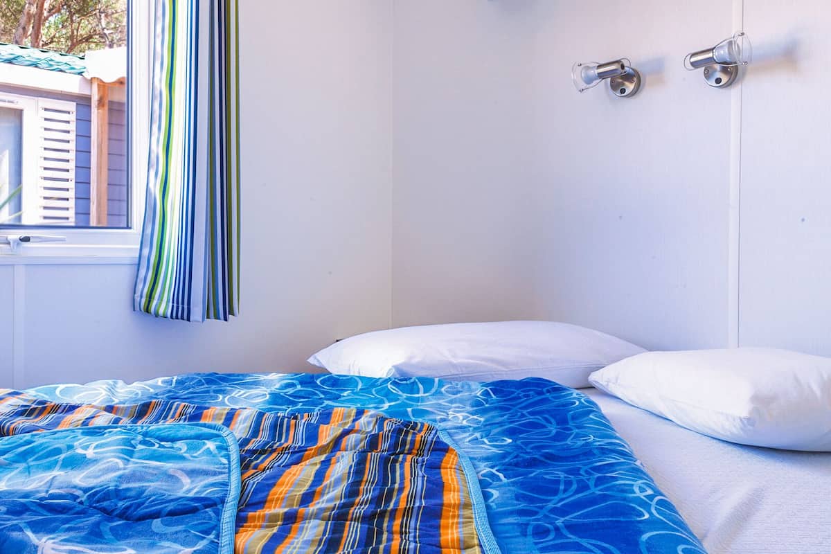 Een slaapkamer met een bed, gestreepte gordijnen, een raam en een houten plank boven het bed.