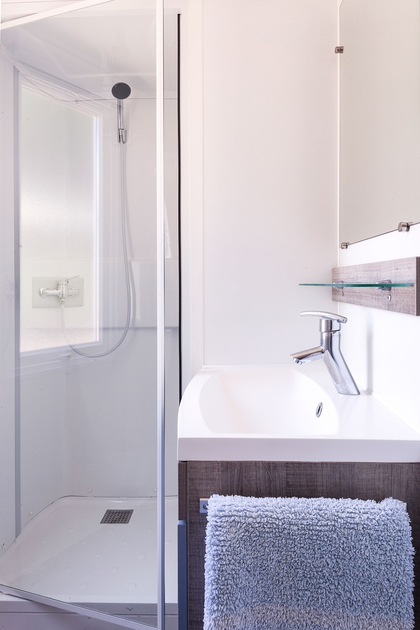 A modern bathroom with a glass shower enclosure, a white sink with a single faucet, and a glass shelf above the sink.