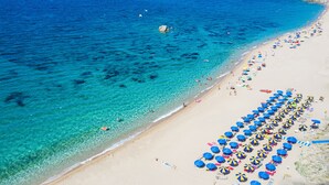 A beach with clear turquoise water, a sandy shore, and numerous colorful umbrellas. - Camping Village Baia Blu La Tortuga (Aglientu)