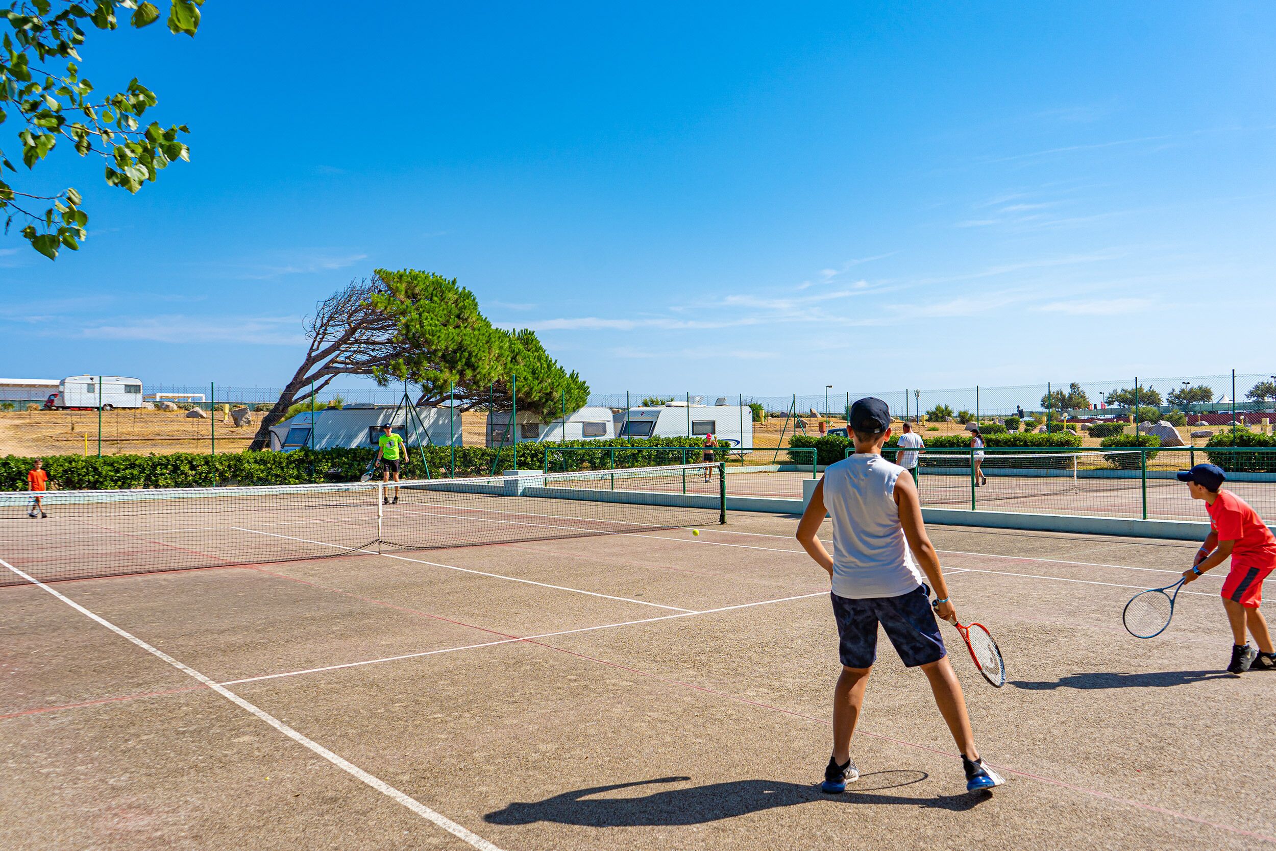 A tennis court with a net, surrounded by a fence, and trees in the background.