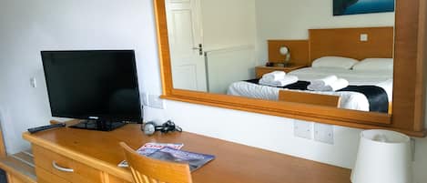 Una habitación de hotel con un escritorio de madera, un televisor, un espejo y una cama con ropa de cama blanca.