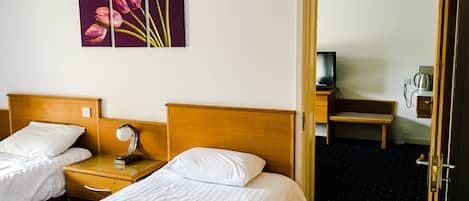 A hotel room with two single beds, a wooden headboard, a nightstand with a lamp, a painting of tulips on the wall, a television, and a coffee maker.