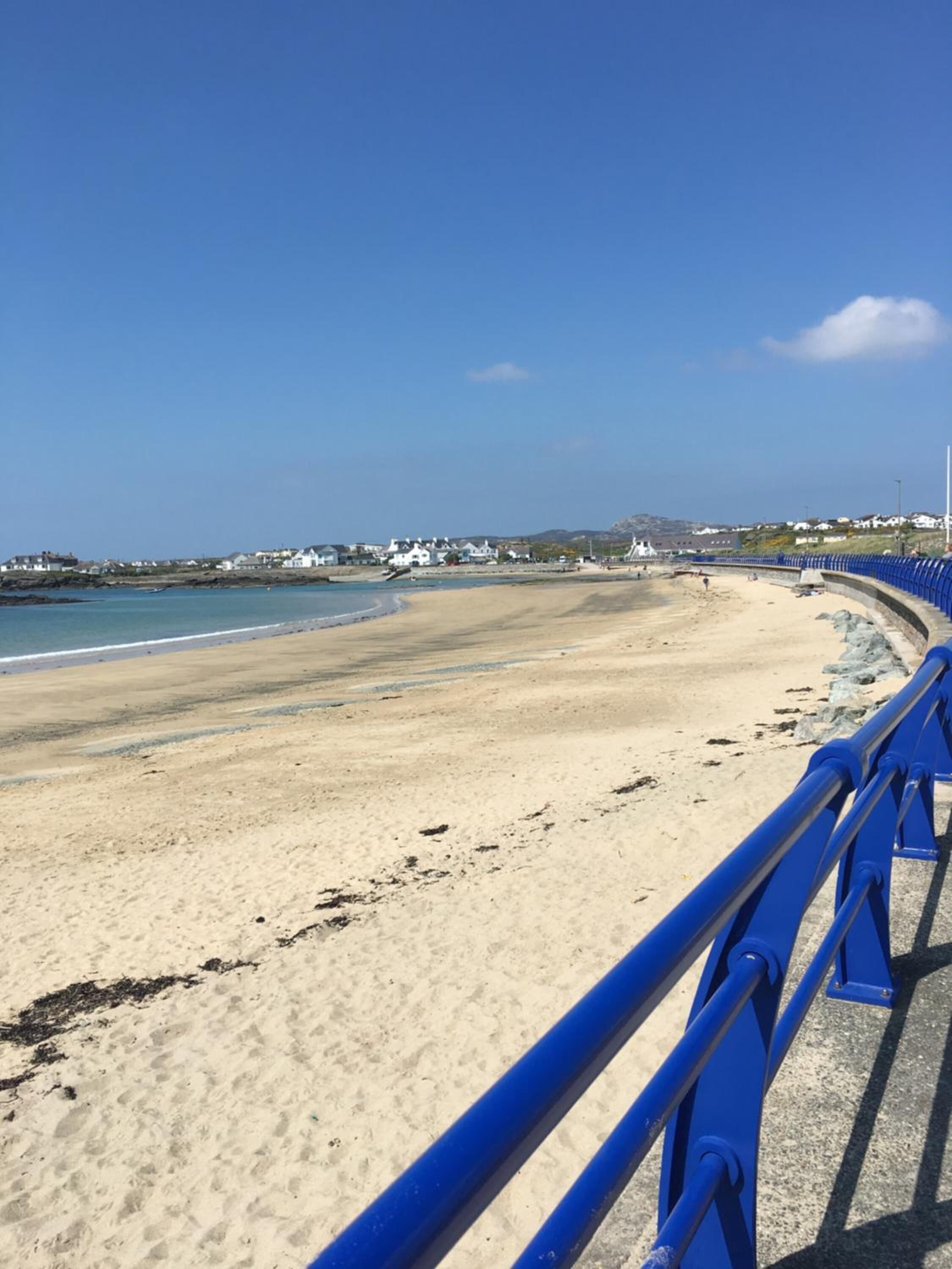 Une plage avec une rambarde bleue, un rivage sablonneux et des maisons en arrière-plan.
