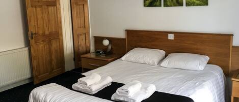 Una cama bien tendida con sábanas blancas, cabecera de madera y mesita de noche con lámpara.