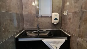 Un baño moderno con un lavamanos negro, un espejo y un dispensador de jabón Gojo.