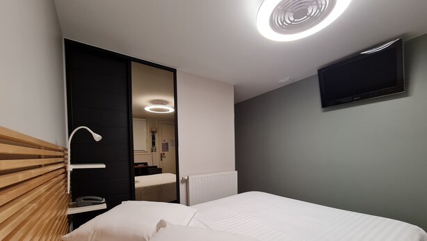 Una habitación de hotel con cama, espejo, televisión y radiador.